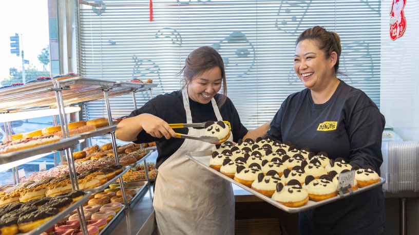 Hermanas trabajando juntas haciendo donuts personalizadas en su pequeña empresa familiar de donuts.