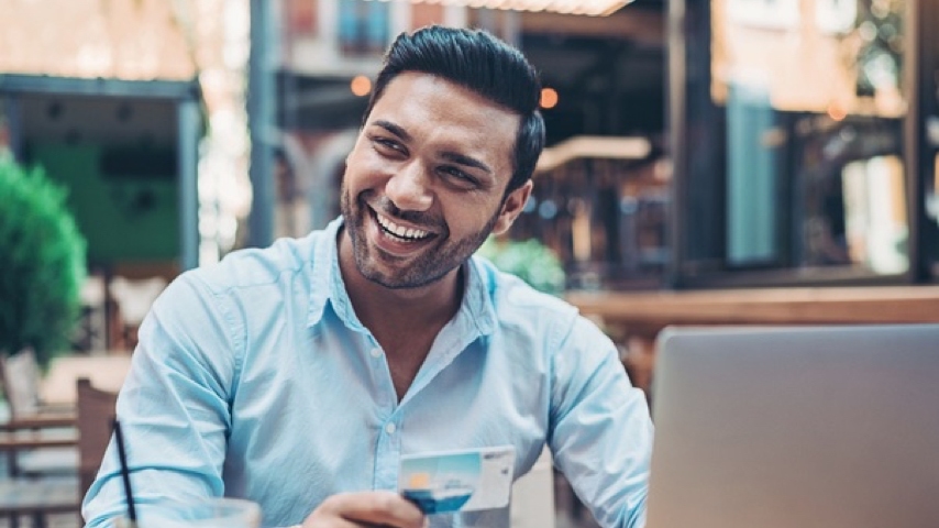 Person sitting down at a table holding a credit card 