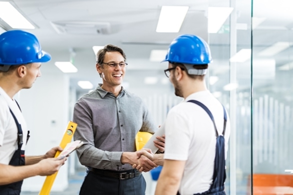 Two people shaking hands while another person stands nearby watching