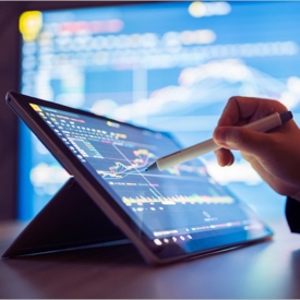 A hand holding a stylus pointing at a tablet displaying a dashboard