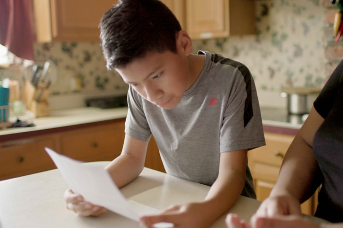 Un niño sentado junto a una familiar mira un documento para traducírselo.