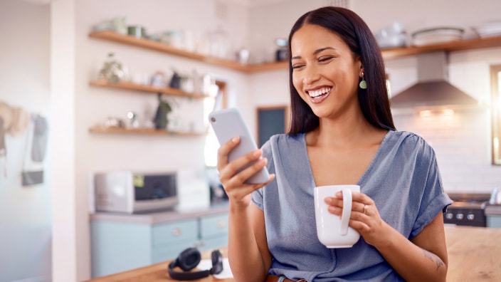 Una joven hispana explora Financial IQ en su teléfono mientras sostiene una taza en su cocina