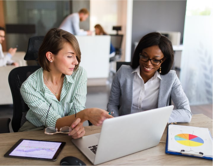 Two women at a desk looking at charts and a computer screen.